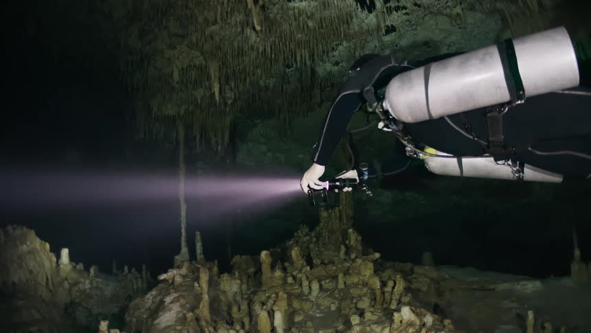 Diver with oxygen cylinders venturing into an aquatic cave