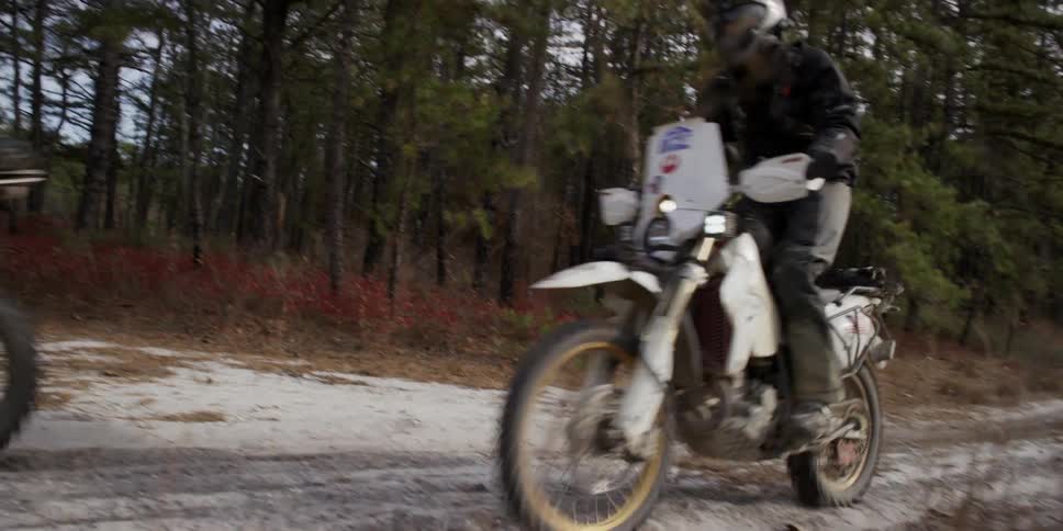 Two people ride motorbikes on a dirt path