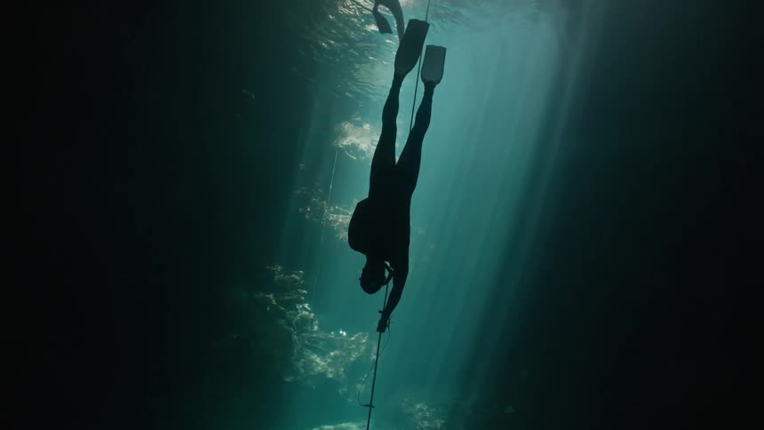 Diver silhouetted in the light from above follows a line while diving deeper into a cave
