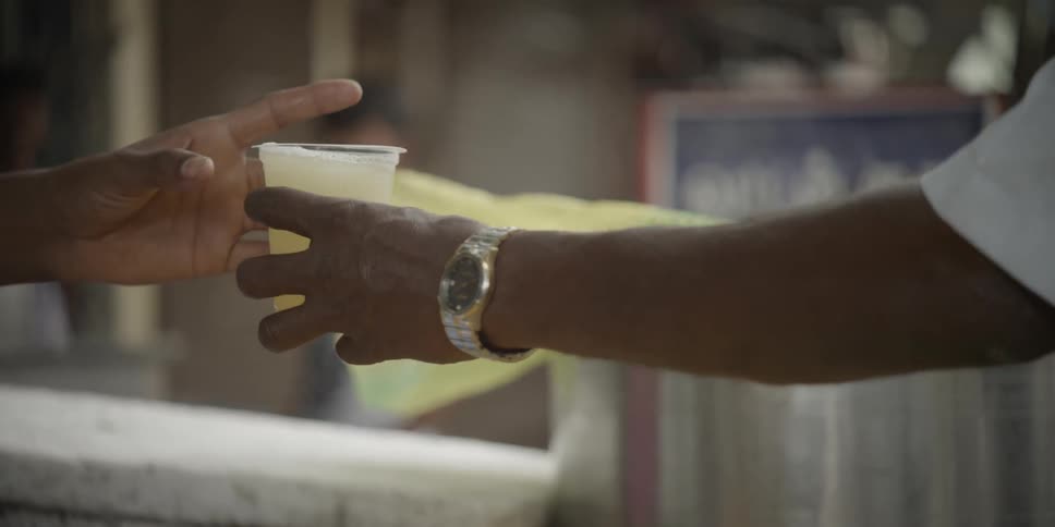 Person receiving a cup of lemonade on a city street and taking a sip