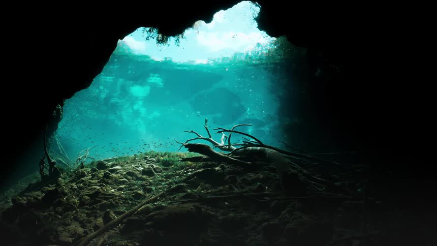Sun shines through the water into the mouth of a cave
