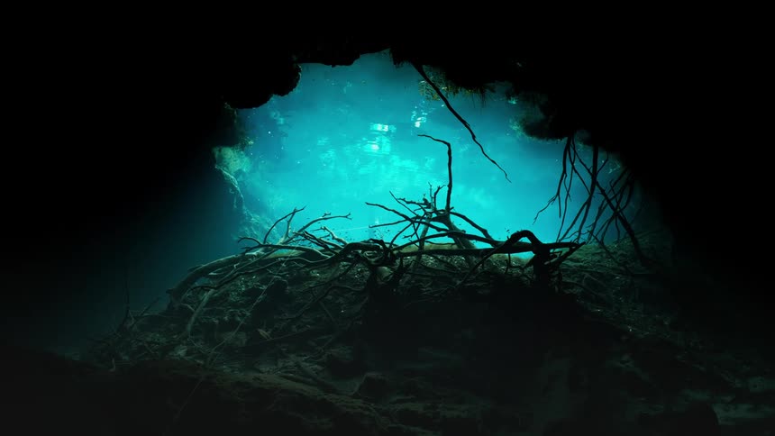 Light illuminates entrance to an underwater cave as air bubbles rise toward the surface