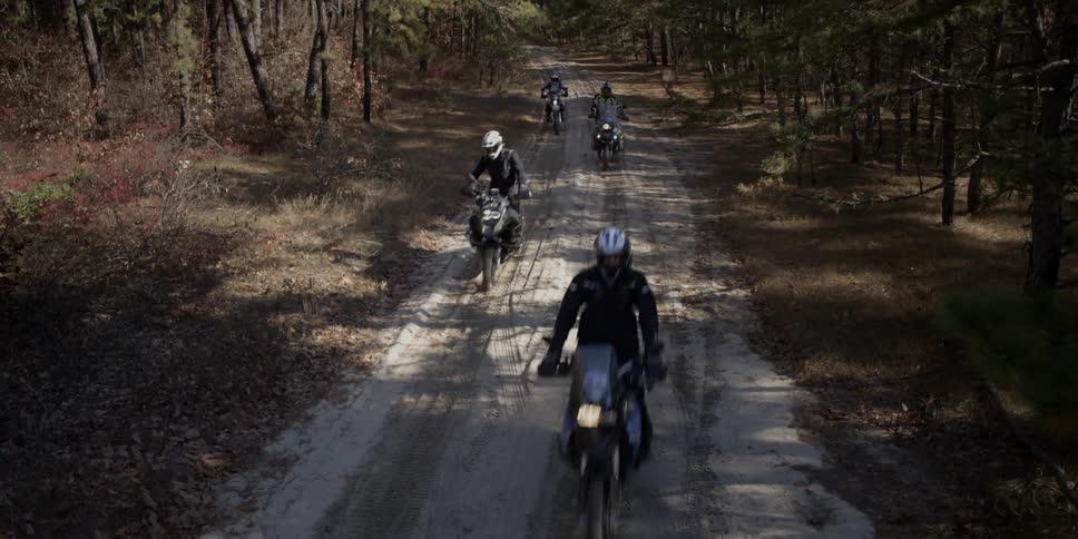 Group of people riding dirt bikes on dirt road in woods