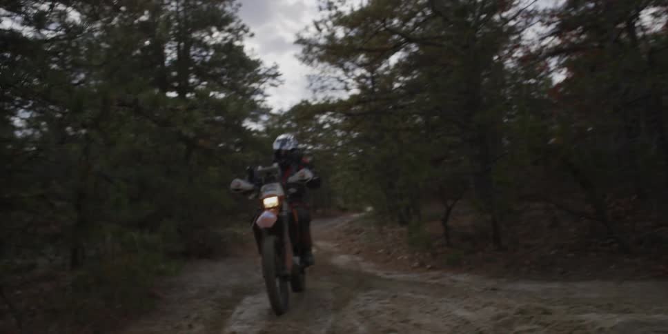 A person rides a motorcycle on a muddy forest trail