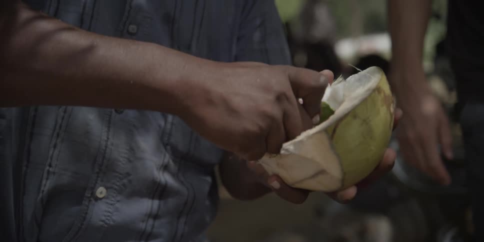 A man is carving flesh from a coconut during the day