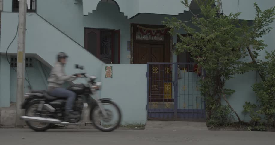 Two people riding motorcycles past a house