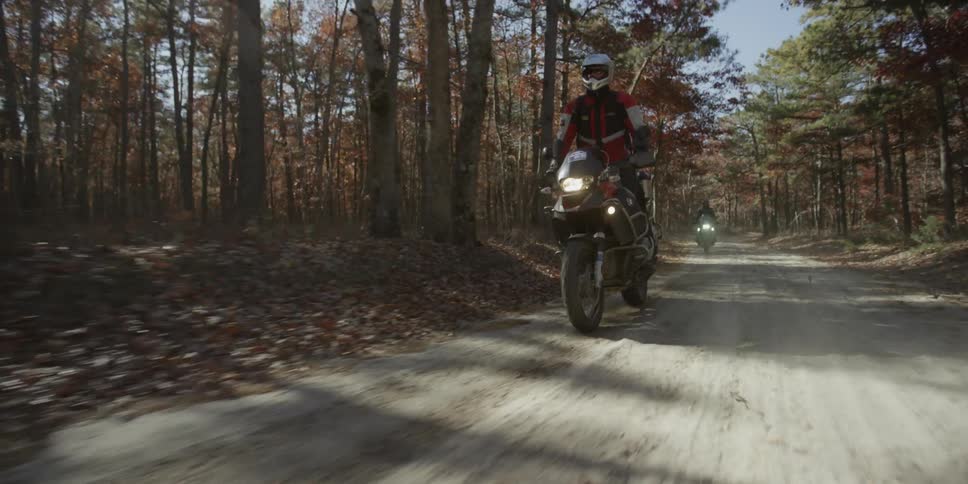 People riding dirt bikes on a dirt road surrounded by trees