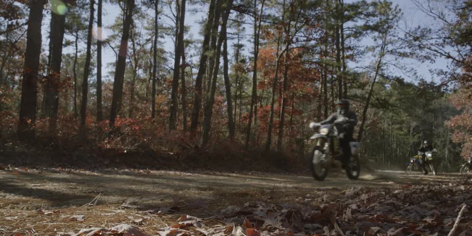 Motorcyclists are riding on a dirt road in a forest