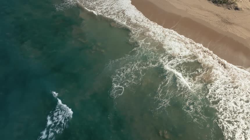 Aerial view of waves crashing in to a sandy beach shore