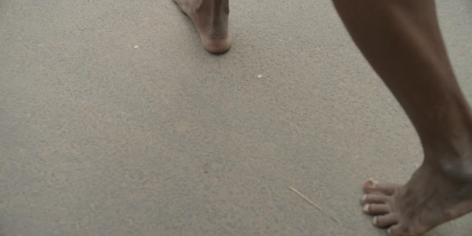 A barefoot man walks on a sidewalk