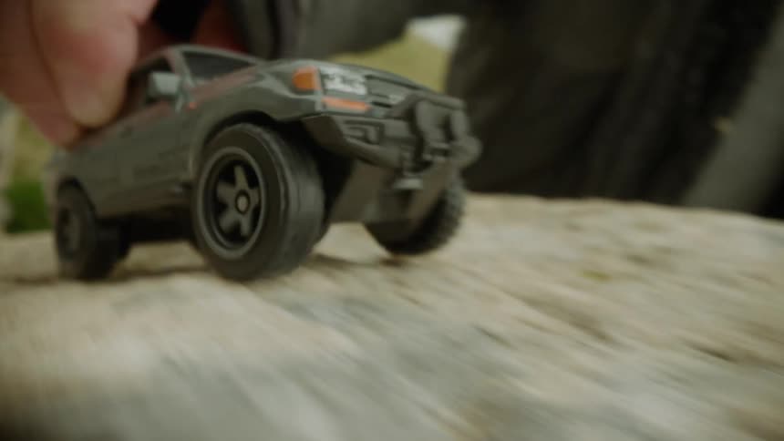 A child is playing with a toy car driving it across a stone