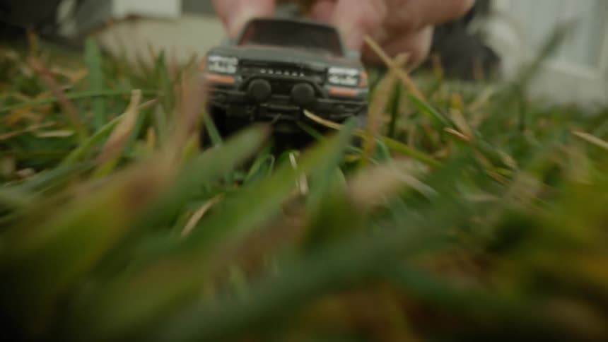 A closeup shot of a person pushing a toy car through grass