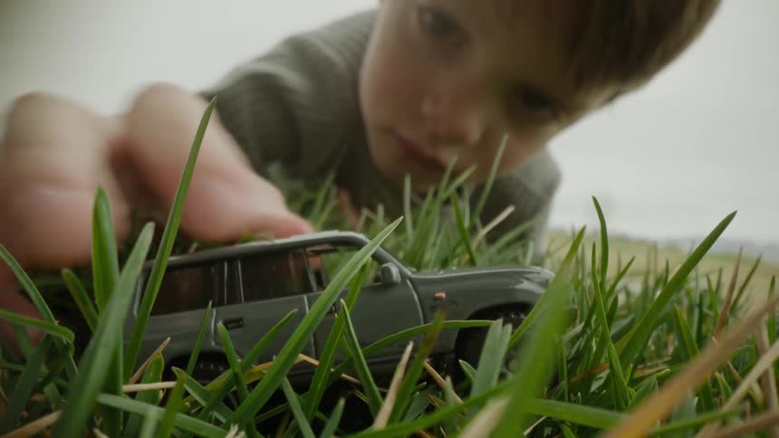 A young boy plays with a grey toy truck in the grass