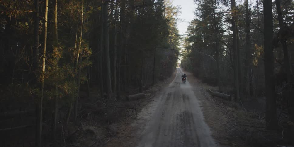 A motorcyclists rides down a narrow road in a forest