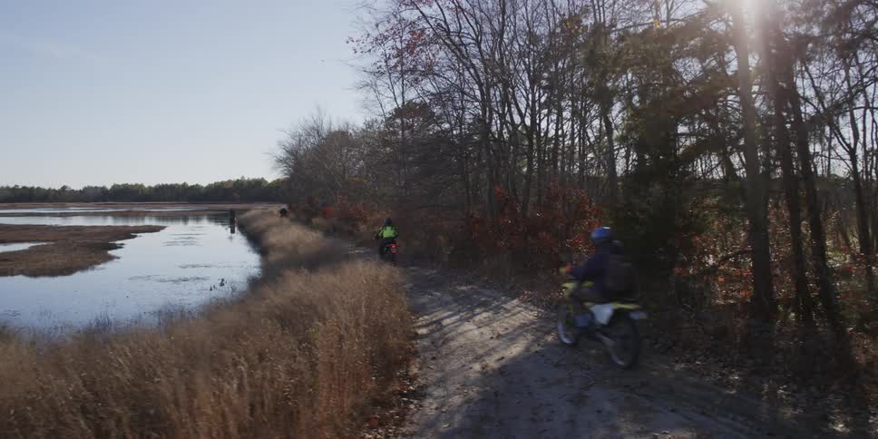 People riding motorcycles down a path next to water