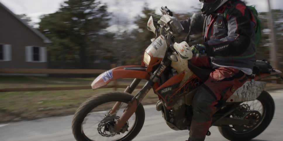 A person on a dirt bike comes out of the woods onto the road
