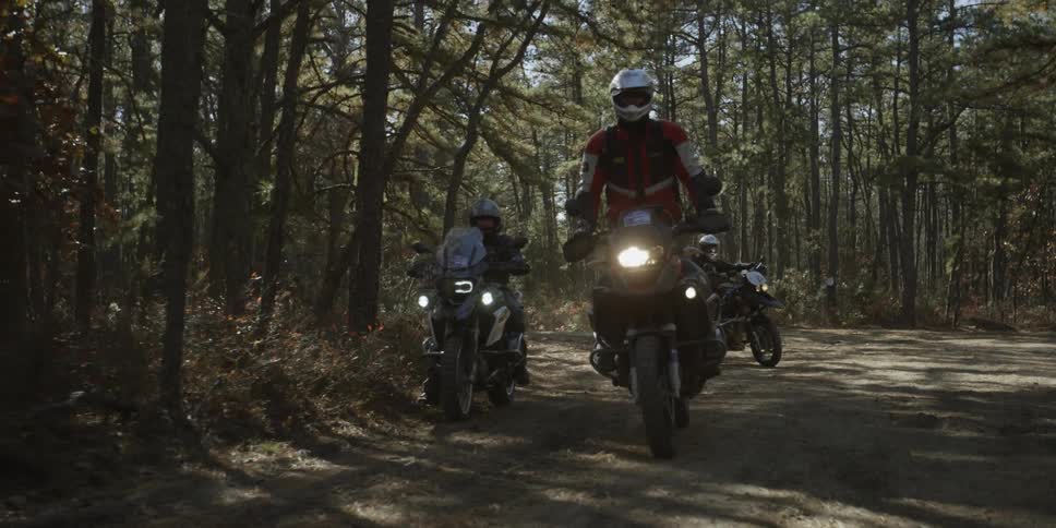 A group of people ride motorcycles through a forest