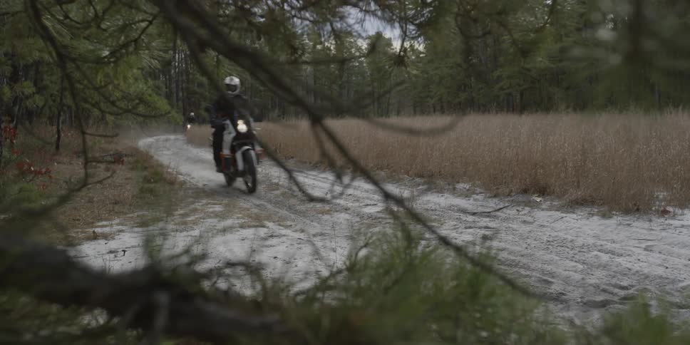 Several people ride motorcycles on a dirt road