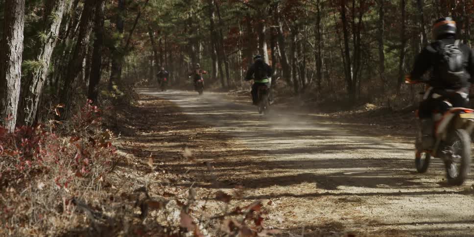 Dirt bike riders ride through a forest trail