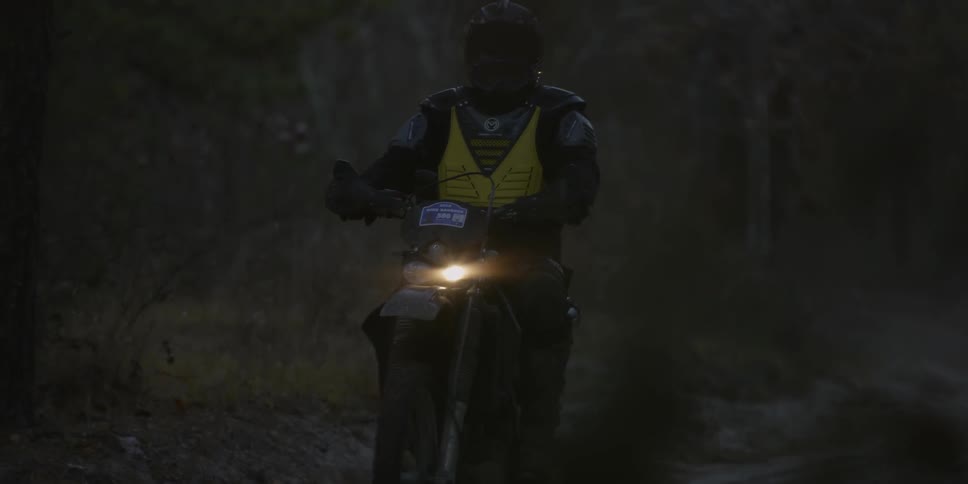 Two people on motorbikes on a dirt road in the evening