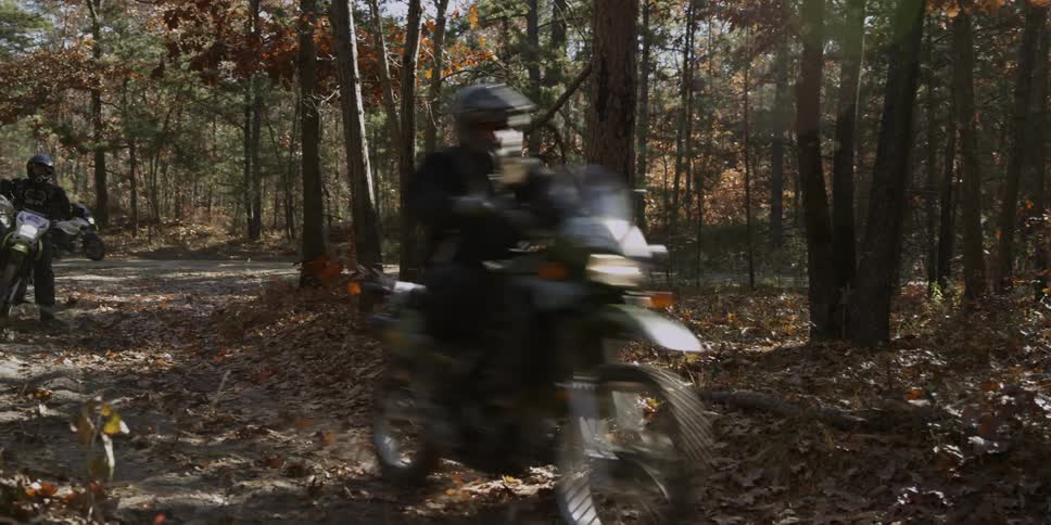 Dirt bike riders ride through a forest trail