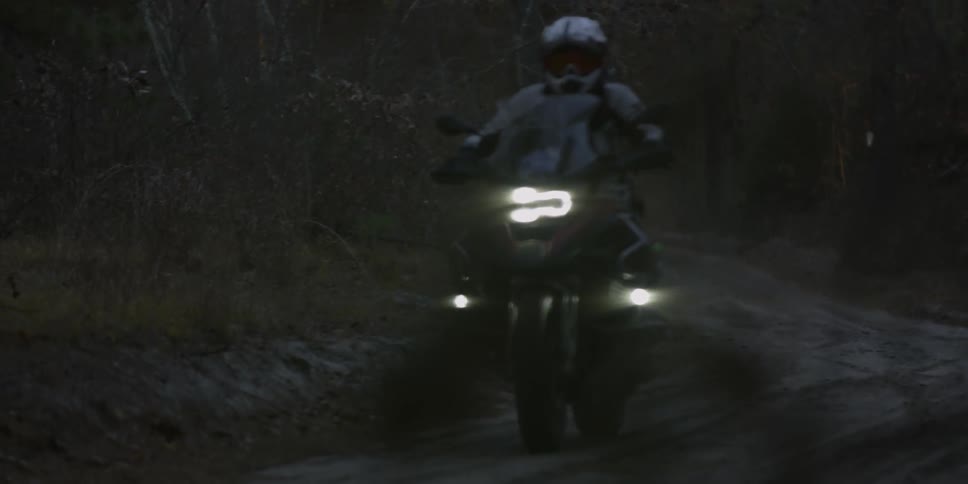 A person rides a motorcycle on a forest trail at dusk