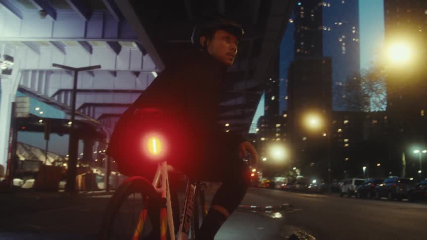 A man wearing a helmet and riding a bicycle with a red light on the back on a street at night