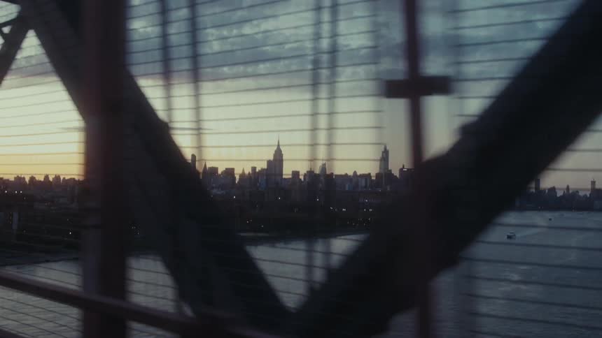 Moving view at dawn of a bridge above a sea canal in a metropolis in the background with large buildings