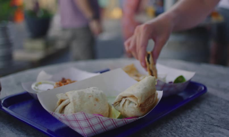 Hands of two people eating a snack at a table with bread and sauces