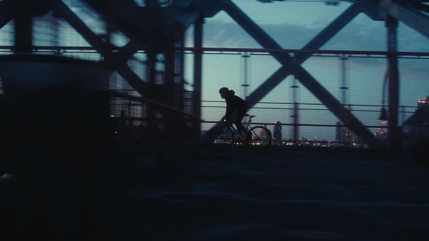 Silhouette of a cyclist riding across a bridge at dawn