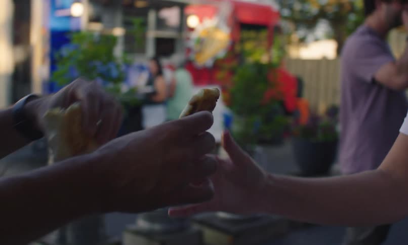 People share food bought at a food truck while standing at an outdoor table