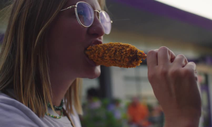 Man and woman stand outdoors near a building and eat fried cheese on a stick