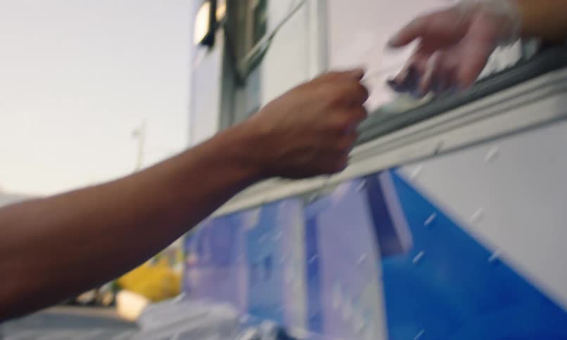 A customer hands a credit card to a worker inside of a food truck