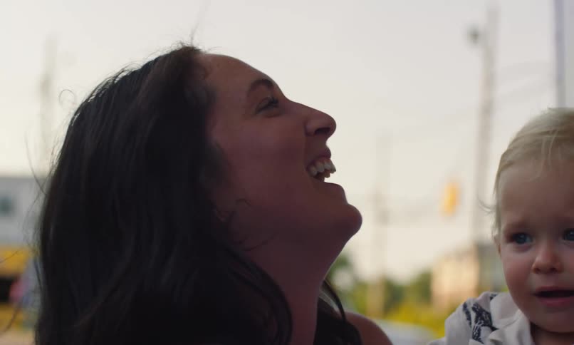A woman holding a baby laughs while standing next to an ice cream truck