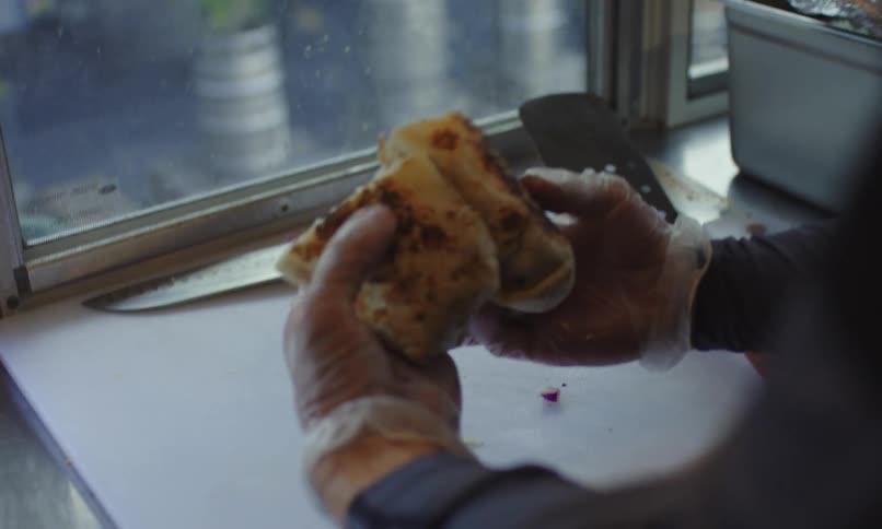 A close up of a persons hands wearing clear plastic gloves holding a sandwich near a window