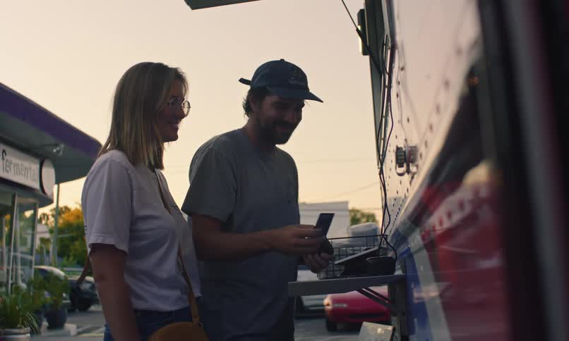Man swiping his card on a machine in a food truck and a woman next to him