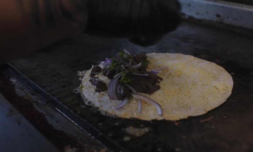 Hand with gloves placing spices on top of a tortilla on a hot griddle