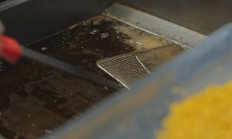 Industrial deep fryer with bubbling oil and a breaded item being fried