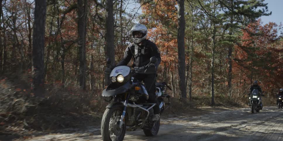 People riding motorcycles down a tree lined street in fall