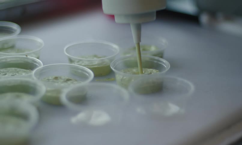 A tube of green sauce filling several small transparent plastic containers