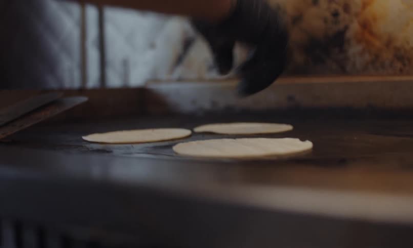Closeup of a hand wearing a black latex glove flipping tortillas over a hot grill