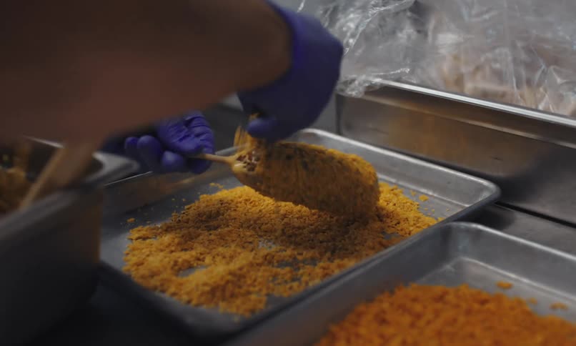 A man wearing blue latex gloves prepares a deep fried food item for a customer