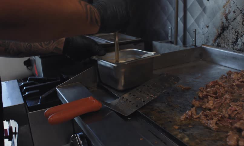 Mixing batter in a metal container while bits of meat cook on a hot metal plate