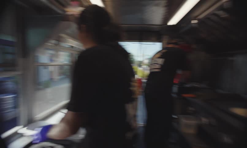 Two workers prepare food inside a food truck