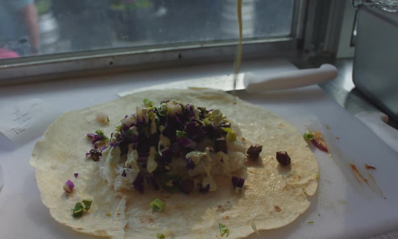 Sauce being poured onto food inside of a tortilla