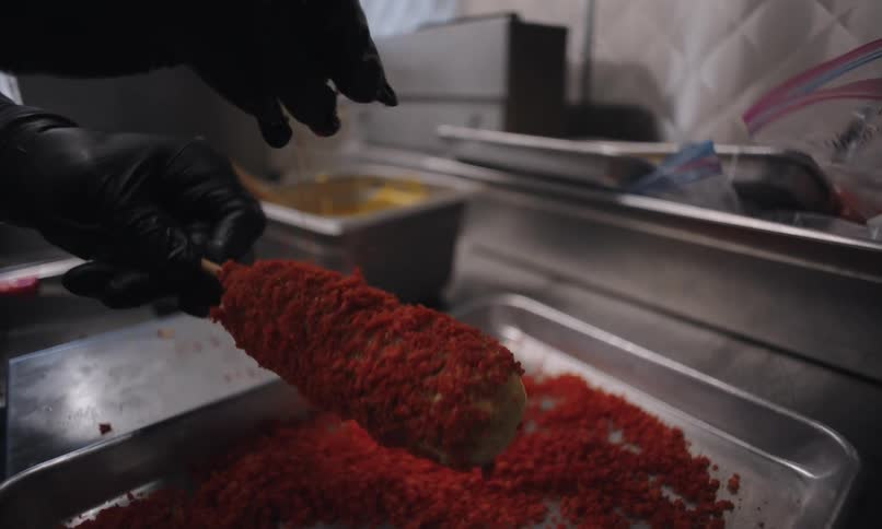 A restaurant employee sprinkles seasonings on a corn dog