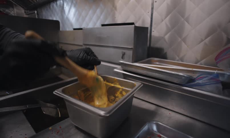 Hand with black glove holds a spatula and spreads a yellow sauce on breaded chicken