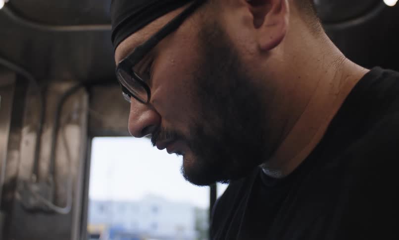 A hispanic man works inside of a food truck in a suburb