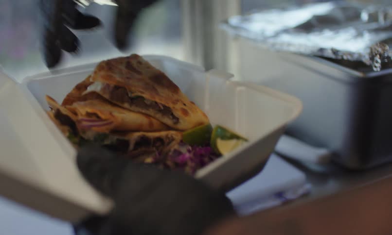 Male food truck worker fills a takeout container with quesadillas