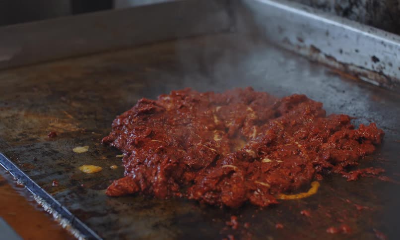 Cook seasons meat they are cooking on a flat cooking surface